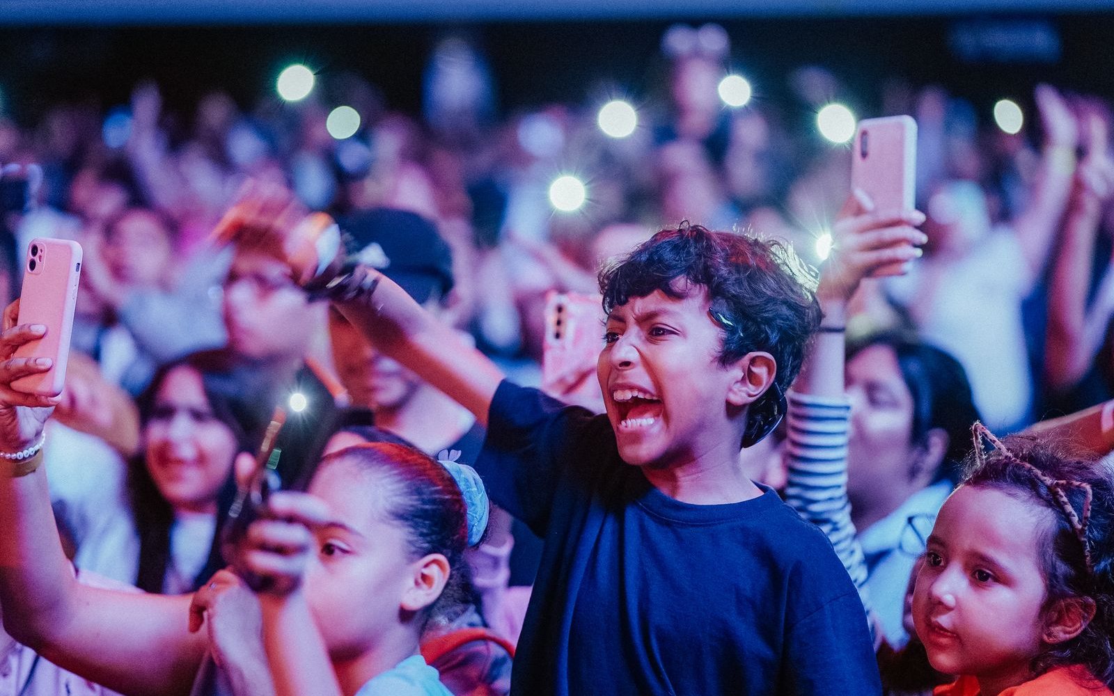 Des enfants vivent un concert, lumières et chansons partagées.